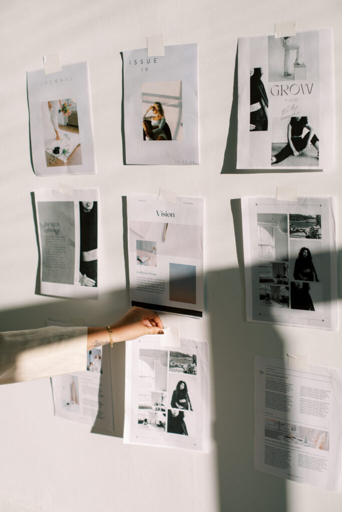 Showit Templates for Photographers | High Tide Strategy Full Service Marketing Agency | A hand places a paper under several magazine pages taped to a white wall. The collage reflects a creative and artistic atmosphere with a focus on fashion and style.