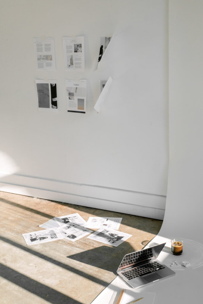 SEO Tips for Photographers | High Tide Strategy Full Service Marketing Agency | A minimalist workspace with a laptop on the floor, surrounded by scattered papers and a lit candle. Papers are also taped to a white wall, conveying a creative and calm atmosphere.