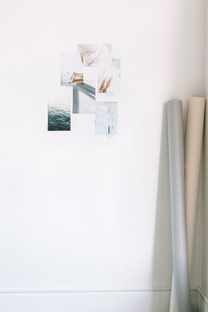 Showit Website Designer for Photographers | High Tide Strategy Full Service Marketing Agency | A white wall displays a collage of serene, minimalist photos featuring ocean waves and pampas grass. Rolls of neutral-toned paper lean against the wall.