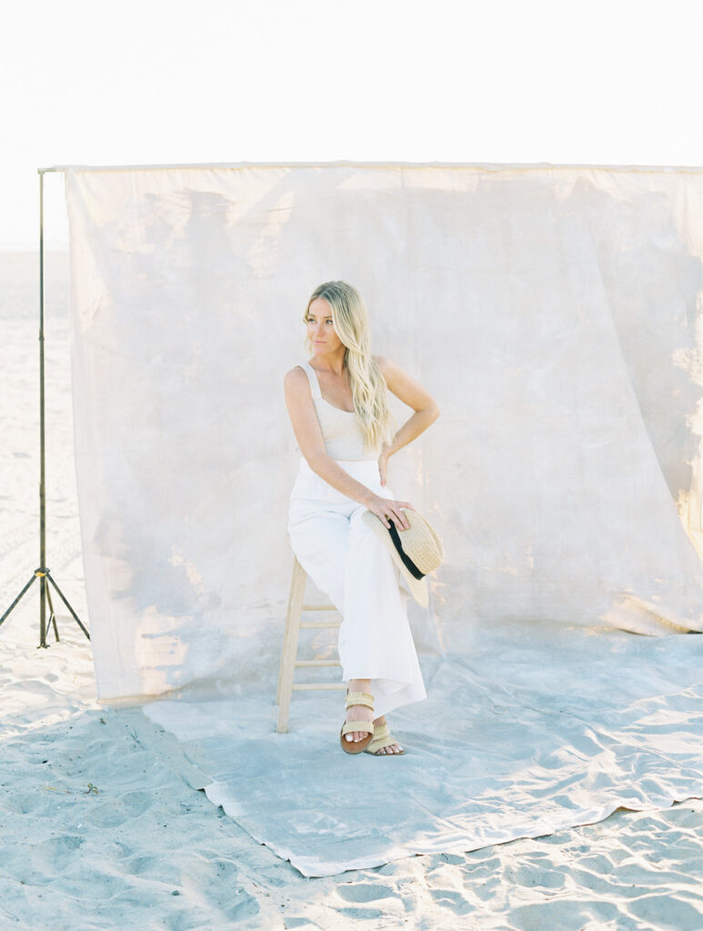 SEO Tips for Photographers | High Tide Strategy Full Service Marketing Agency | Mandy in a white outfit sits on a stool on a beach, with a neutral backdrop and soft lighting. 