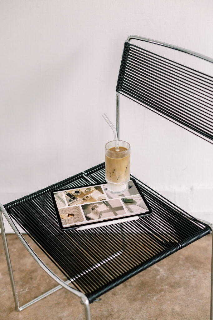 Showit Brand and Website Designers | High Tide Strategy Full Service Marketing Agency | A sleek black wire chair holds an iced coffee and a tablet displaying photos. The setting is minimalist and relaxed, evoking a sense of calm and focus.