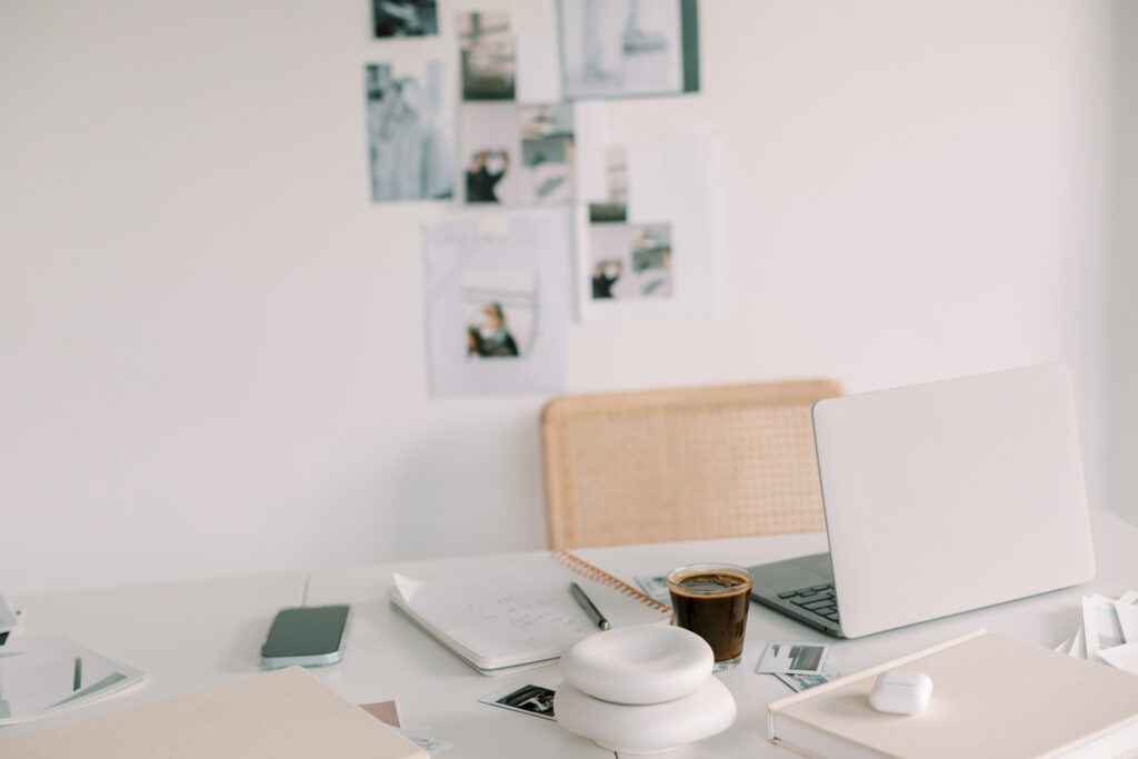 Showit Templates for Wedding Photographers | High Tide Strategy Full Service Marketing Agency | A minimalist workspace features a closed laptop, a smartphone, a notepad, and a coffee cup on a white desk. Photos are pinned to the wall, giving an inspiring feel.
