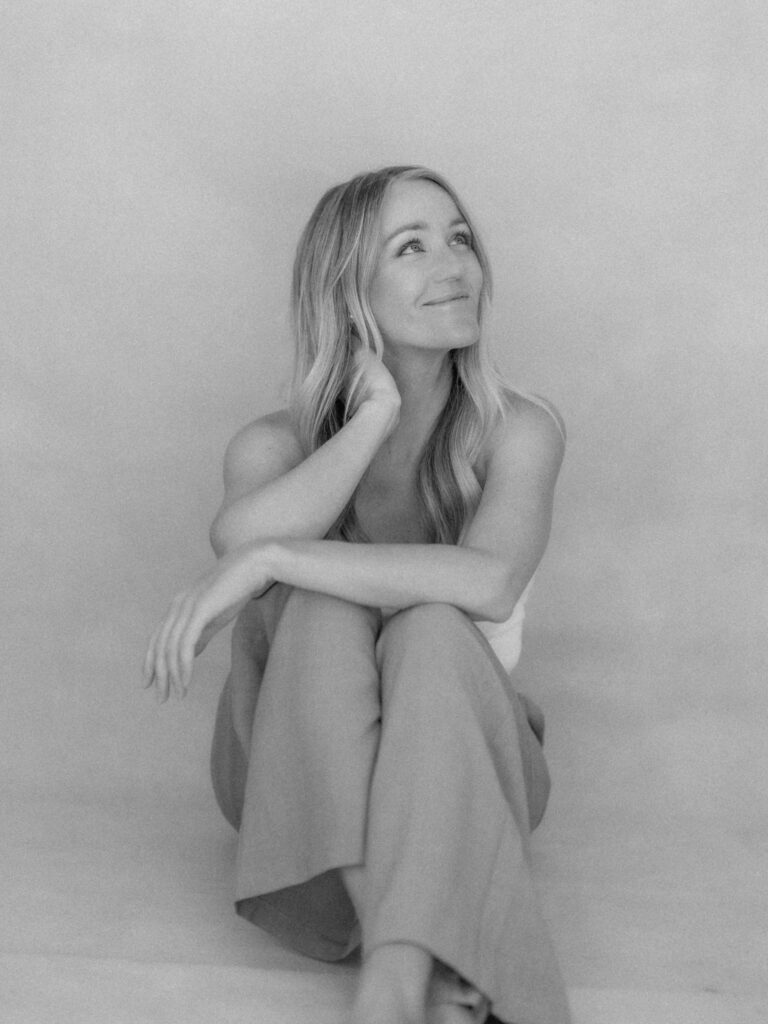 SEO Tips for Photographers | High Tide Strategy Full Service Marketing Agency | Black and white photo of Mandy sitting cross-legged, looking up thoughtfully.