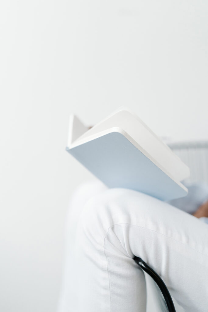 SEO Expert for Photographers | High Tide Strategy Full Service Marketing Agency | A person in white pants sits on a chair reading a book, with focus on the open pages and their knee. The scene conveys a calm, minimalist vibe.