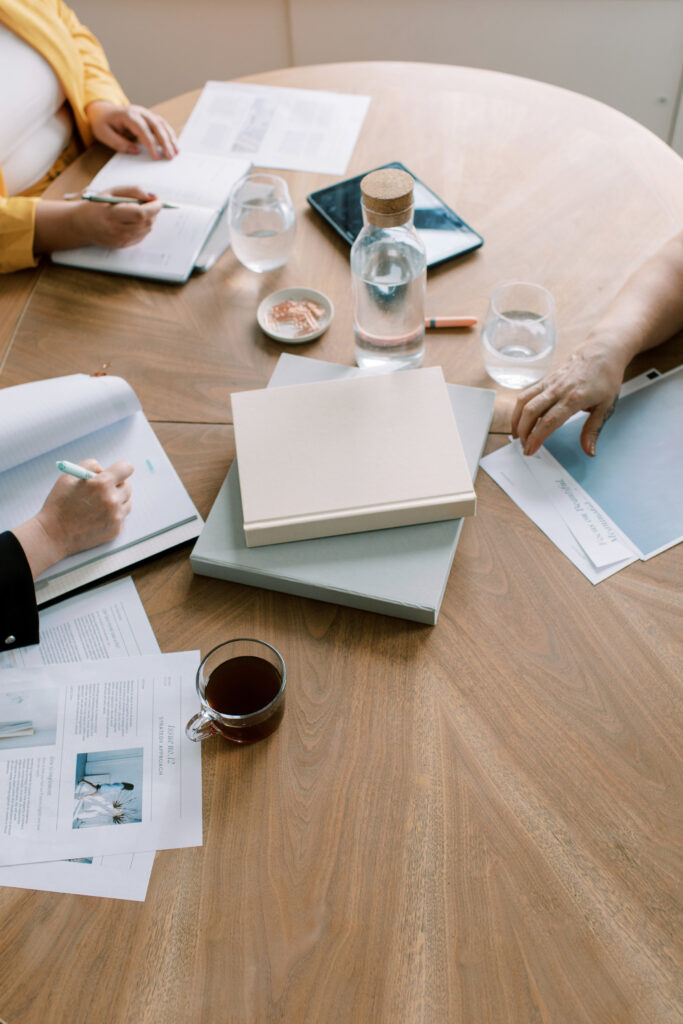 SEO for Fine Art Photographers | High Tide Strategy Full Service Marketing Agency | People working around a wooden table with notebooks, papers, a tablet, glasses of water, and a coffee cup, conveying a collaborative, focused atmosphere.