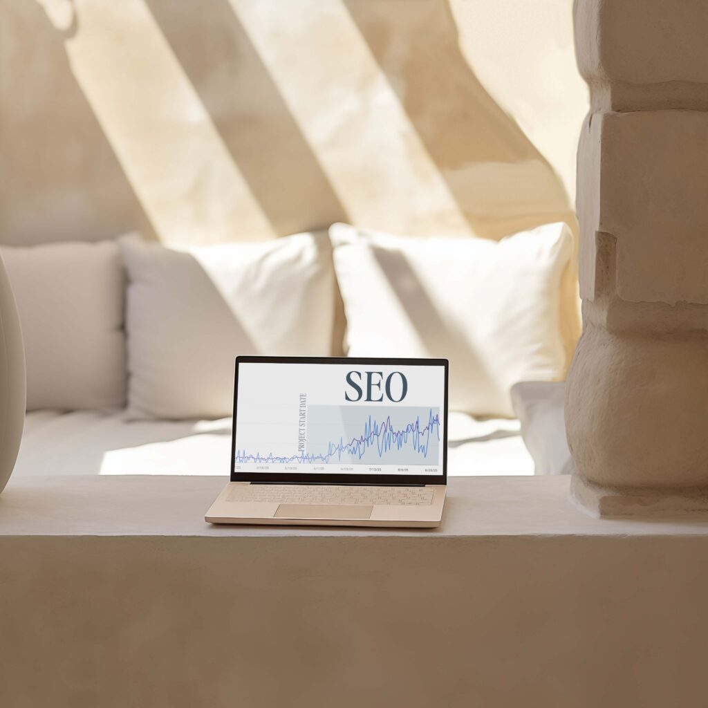 Local SEO for Photographers | High Tide Strategy Full Service Marketing Agency | A laptop sits on a sunlit ledge displaying an SEO chart. The background features a soft, beige, cozy sofa and rustic stone wall, creating a serene ambiance.