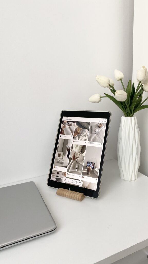 Marketing for Interior Designers | High Tide Strategy Full Service Marketing Agency | A tablet displaying a Pinterest board on a white desk, alongside a closed laptop. A white vase with tulips adds a minimalistic, modern touch.