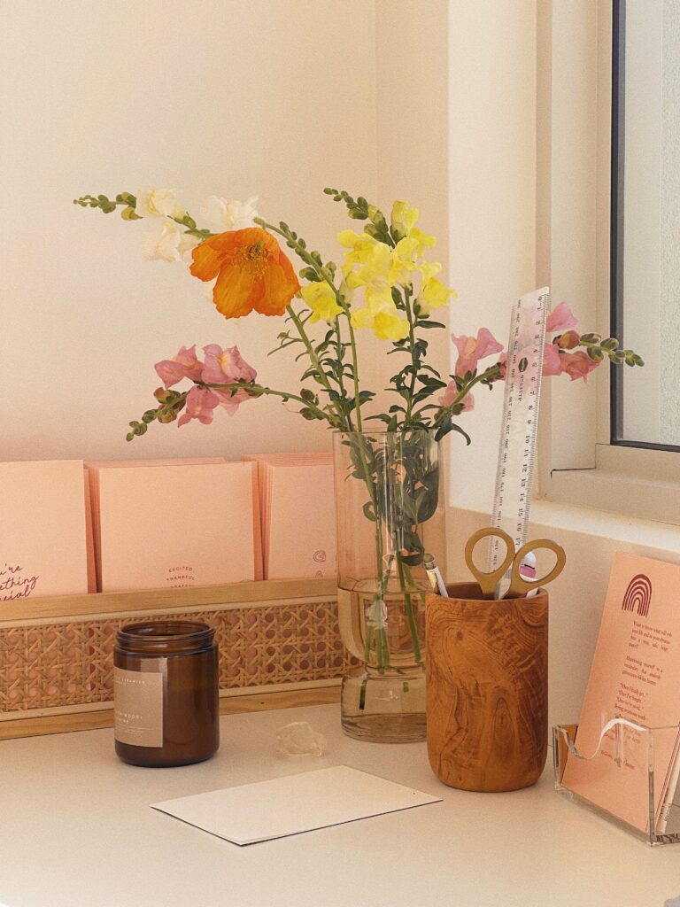 SEO for Florist | High Tide Strategy Full Service Marketing Agency | A cozy desk scene with a vase of vibrant flowers, including orange poppies and pink snapdragons. Nearby are pink stationery, a candle, and wooden pen holder.