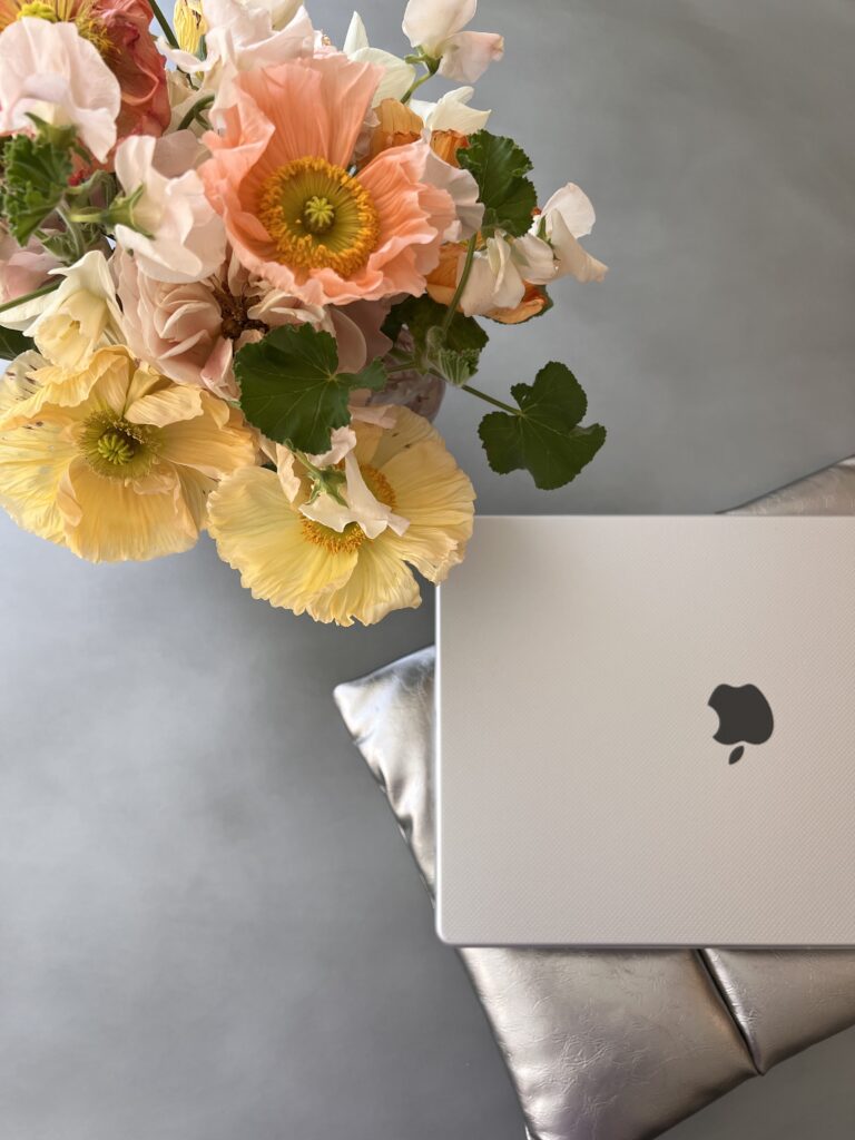Marketing Strategies for Florist Business | High Tide Strategy Full Service Marketing Agency | A bouquet of pink and yellow poppies in a vase next to a silver laptop on a metallic cushion, against a soft gray background. The scene conveys a calm, elegant atmosphere.
