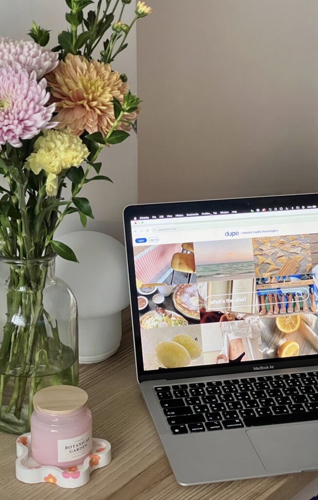 Marketing for Florists | High Tide Strategy Full Service Marketing Agency | A laptop displays a colorful webpage beside a vase of pastel flowers on a desk. A pink candle adds a cozy touch, creating a calm and inviting atmosphere.