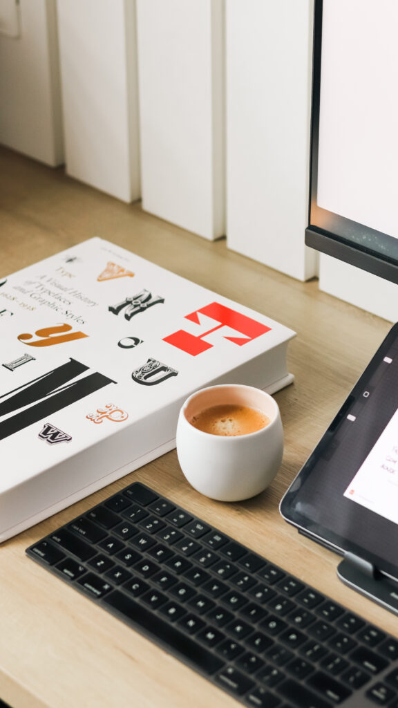 Interior Design Marketing Strategies | High Tide Strategy Full Service Marketing Agency | A minimal desk features a typography book and a white cup of espresso beside a tablet and keyboard. The scene conveys a calm, productive workspace.