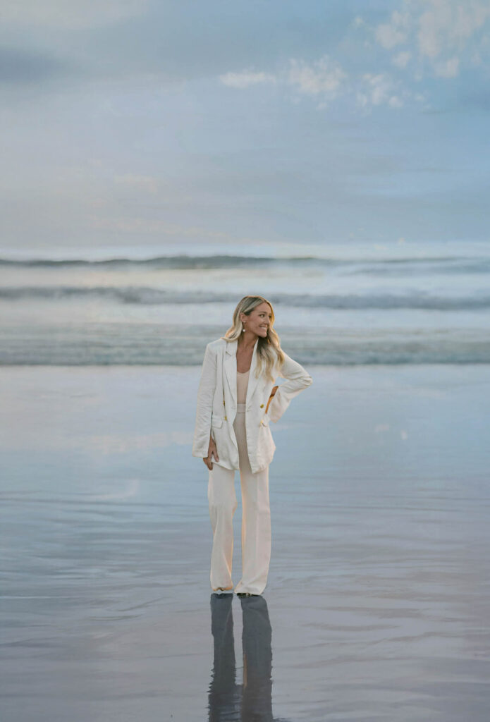 Mandy Ford of High Tide Strategy standing by the ocean in a white pantsuit.