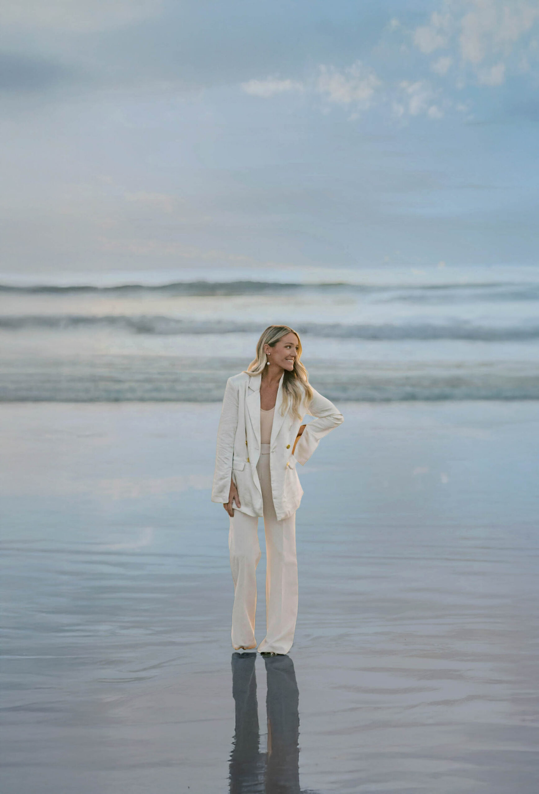 Mandy Ford of High Tide Strategy standing by the ocean in a white pantsuit.