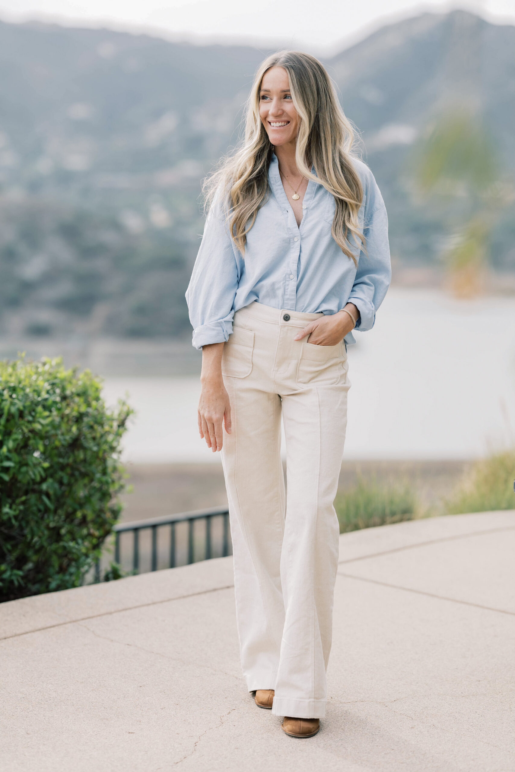 Mandy Ford SEO Expert For Photographers Stands In Front Of A California Mountainside In A Blue Top and White Pants