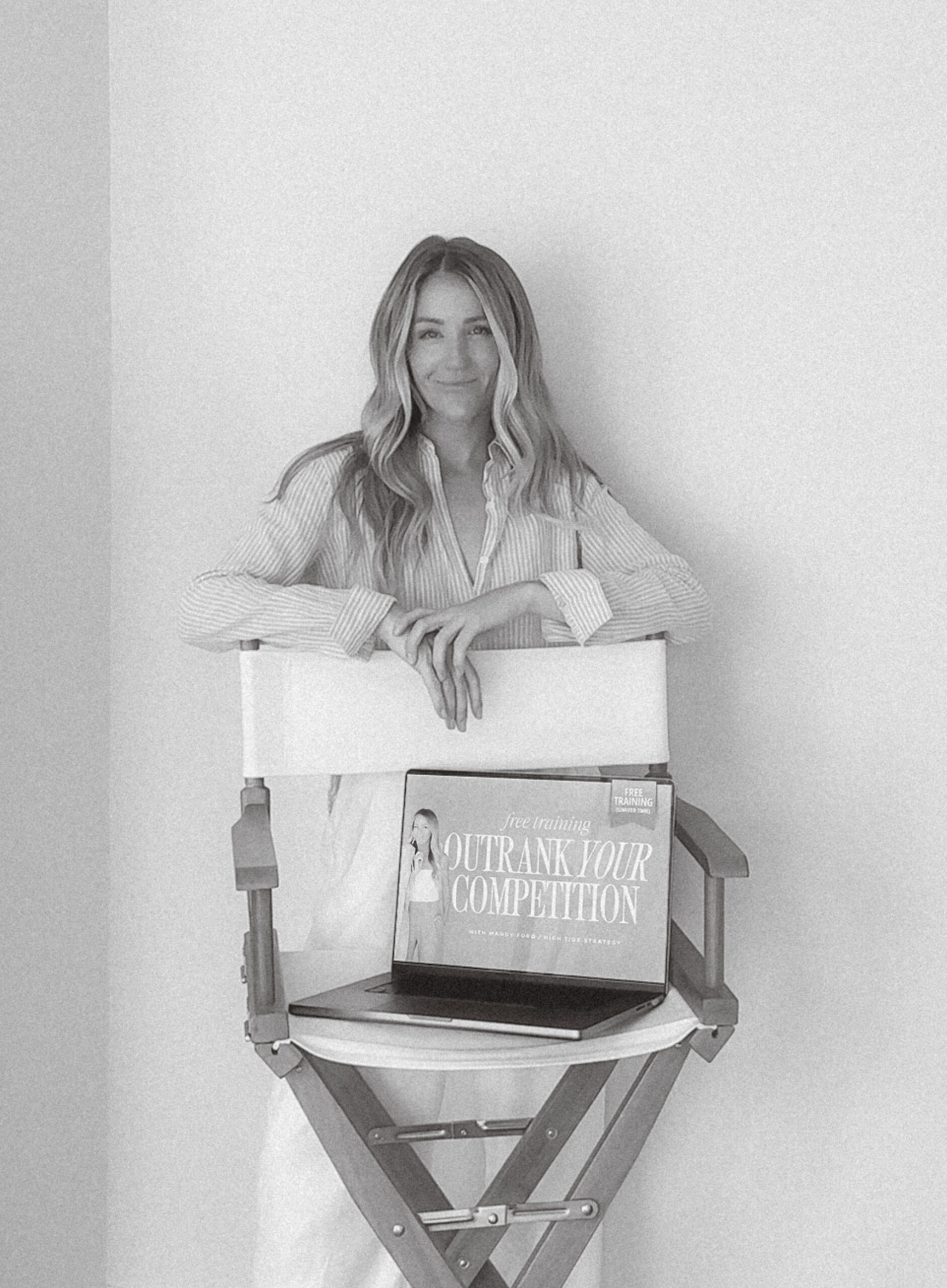Mandy from High Tide Strategy stands behind a white chair with an open laptop showing a curated website optimized for brand visibility.